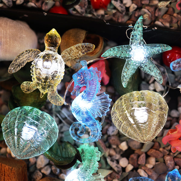 Close-up of translucent sea turtle, seahorse, starfish and shell fairy lights on a pebble display